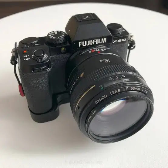 Бездзеркальна камера Fujifilm X-S10 зі встановленим адаптером Viltrox EF-FX2 та об'єктивом Canon EF 50mm f/1.4 на білому столі